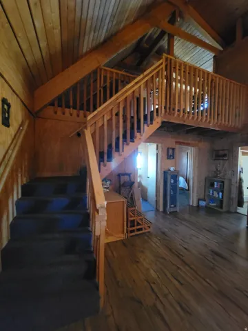 Vaulted wood-paneled ceilings with exposed beams, wood-finish flooring, and a carpeted staircase with a wood railing