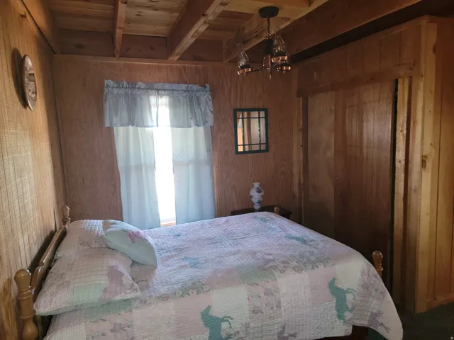 Wood-paneled room featuring a window with light-colored drapes, exposed ceiling beams, a sliding wood door, and a multi-arm ceiling light fixture
