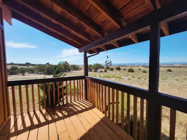 Covered wooden porch with exposed rafters, wood flooring, and a wooden railing