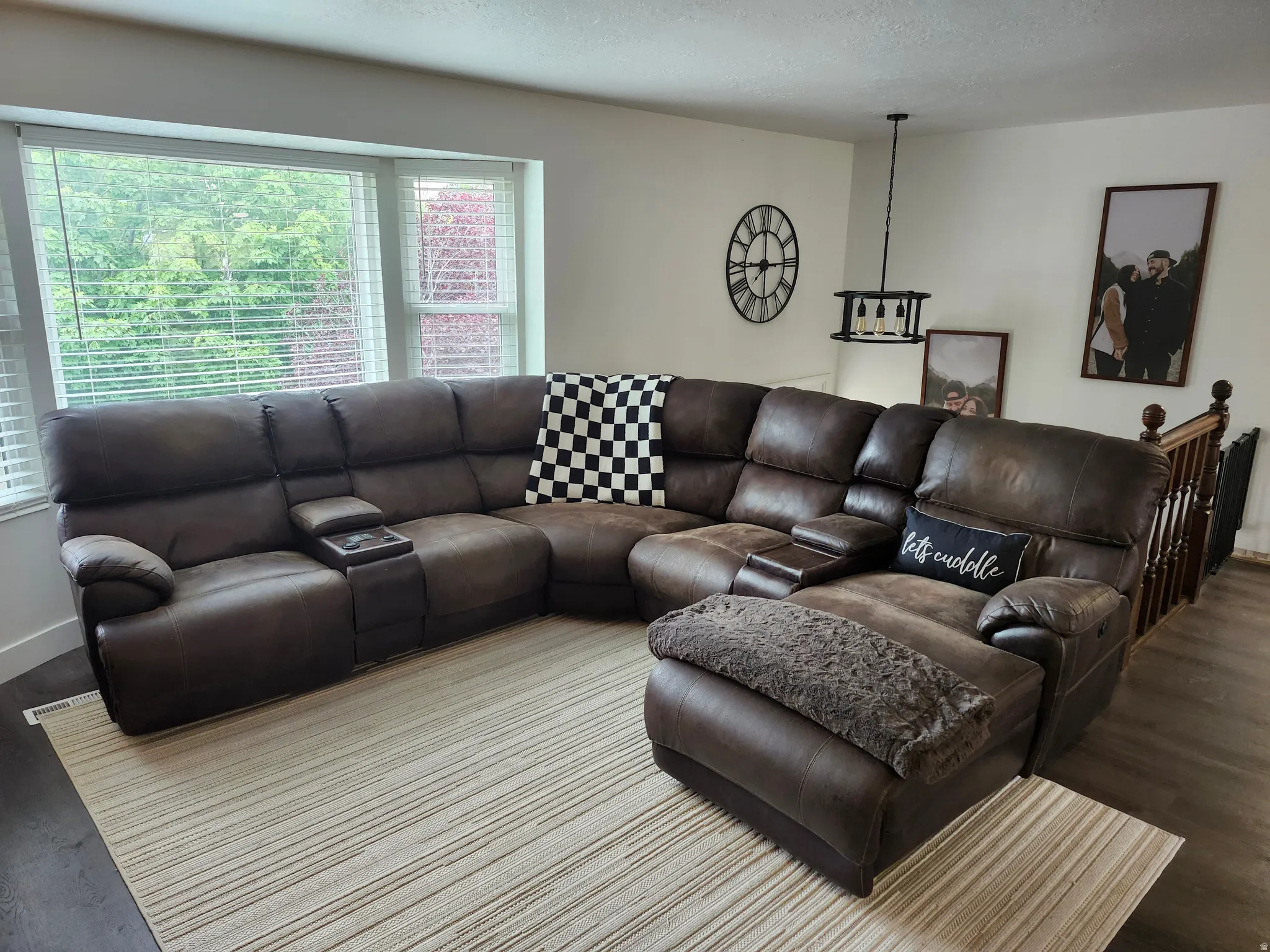 Living area featuring LVP flooring, a contemporary ceiling light fixture, a bay window with blinds, and white wall finishes