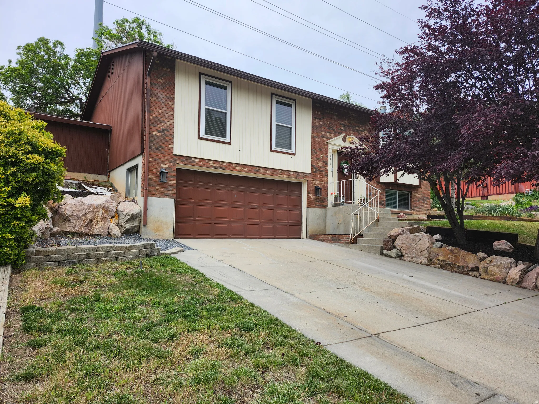 Split-level residence featuring brick and siding exterior, an integrated two-car garage with a brown door, and a concrete driveway