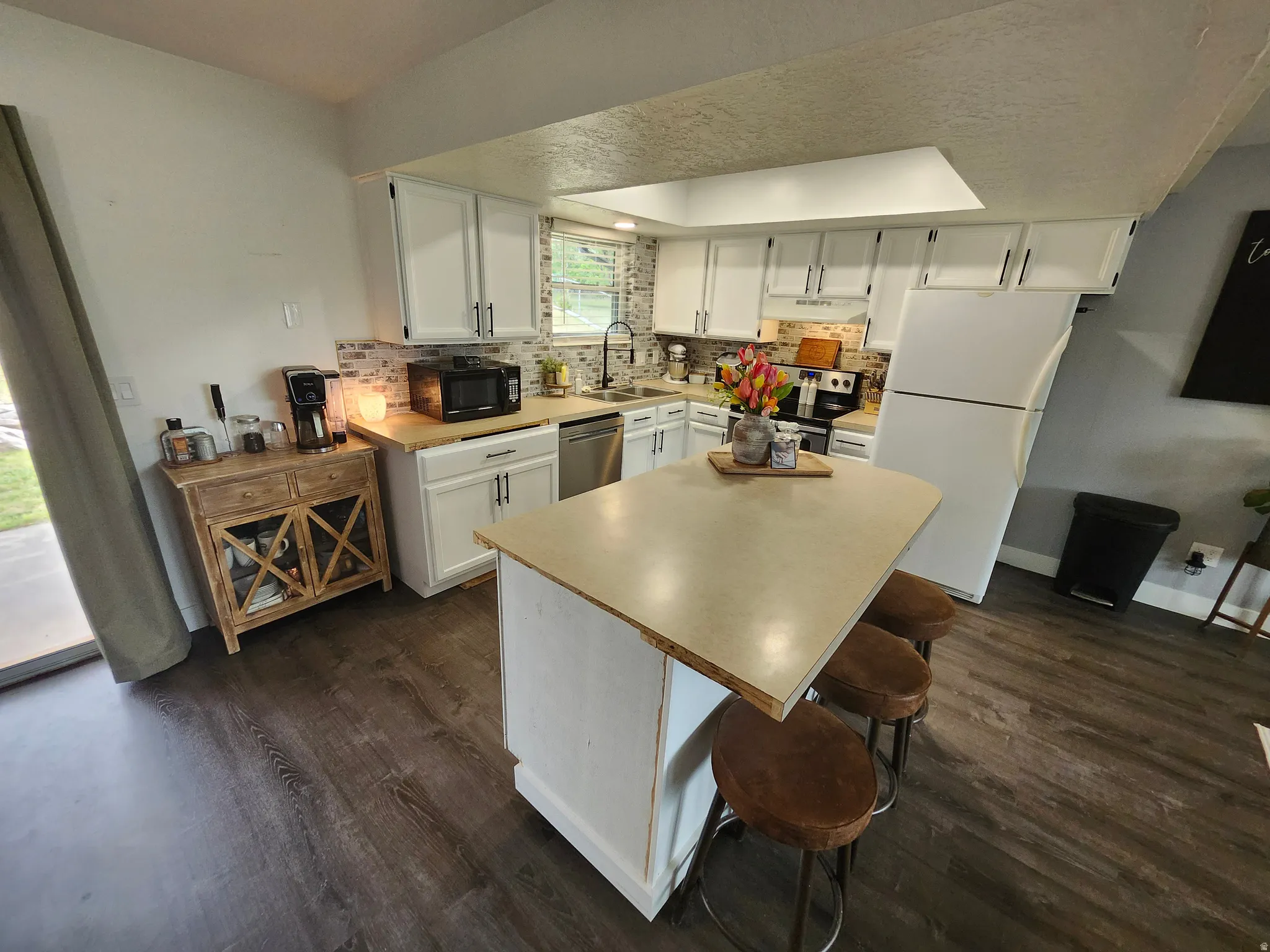 Kitchen with dark wood-finish flooring, white cabinetry, light countertops, and a subway tile backsplash