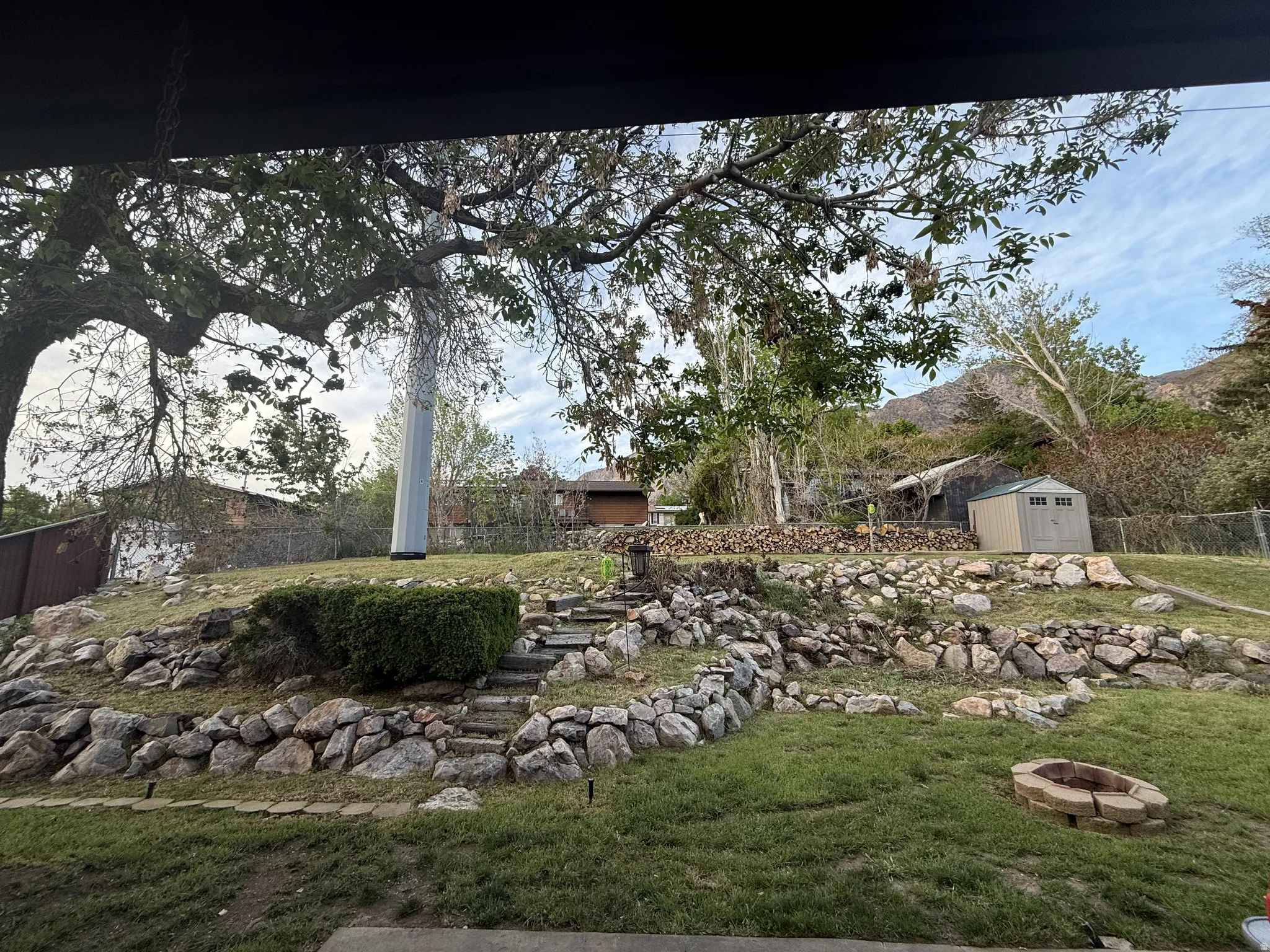 Expansive terraced backyard featuring natural stone retaining walls, a built-in stone fire pit, and mature trees