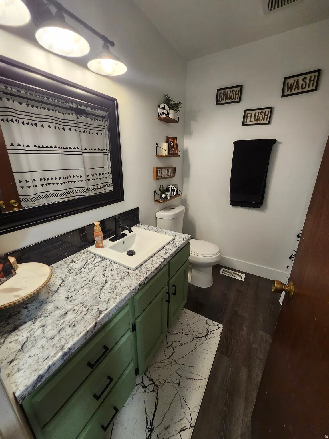 Bathroom featuring a green vanity with a white countertop and integrated sink, dark wood-finish flooring, and a large wall-mounted mirror