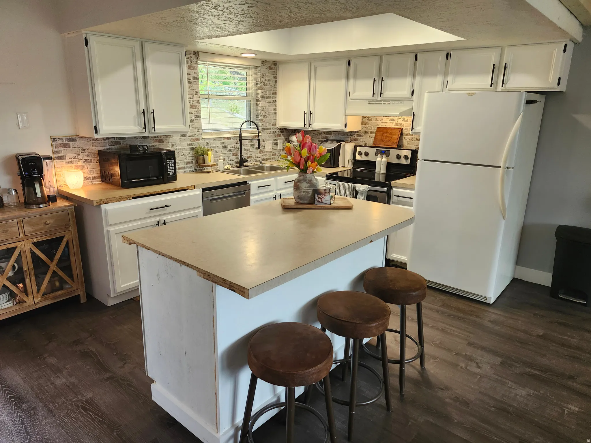 Kitchen featuring an island with seating, white cabinetry with dark hardware, wood-finish countertops, a brick-patterned backsplash, and LVP flooring