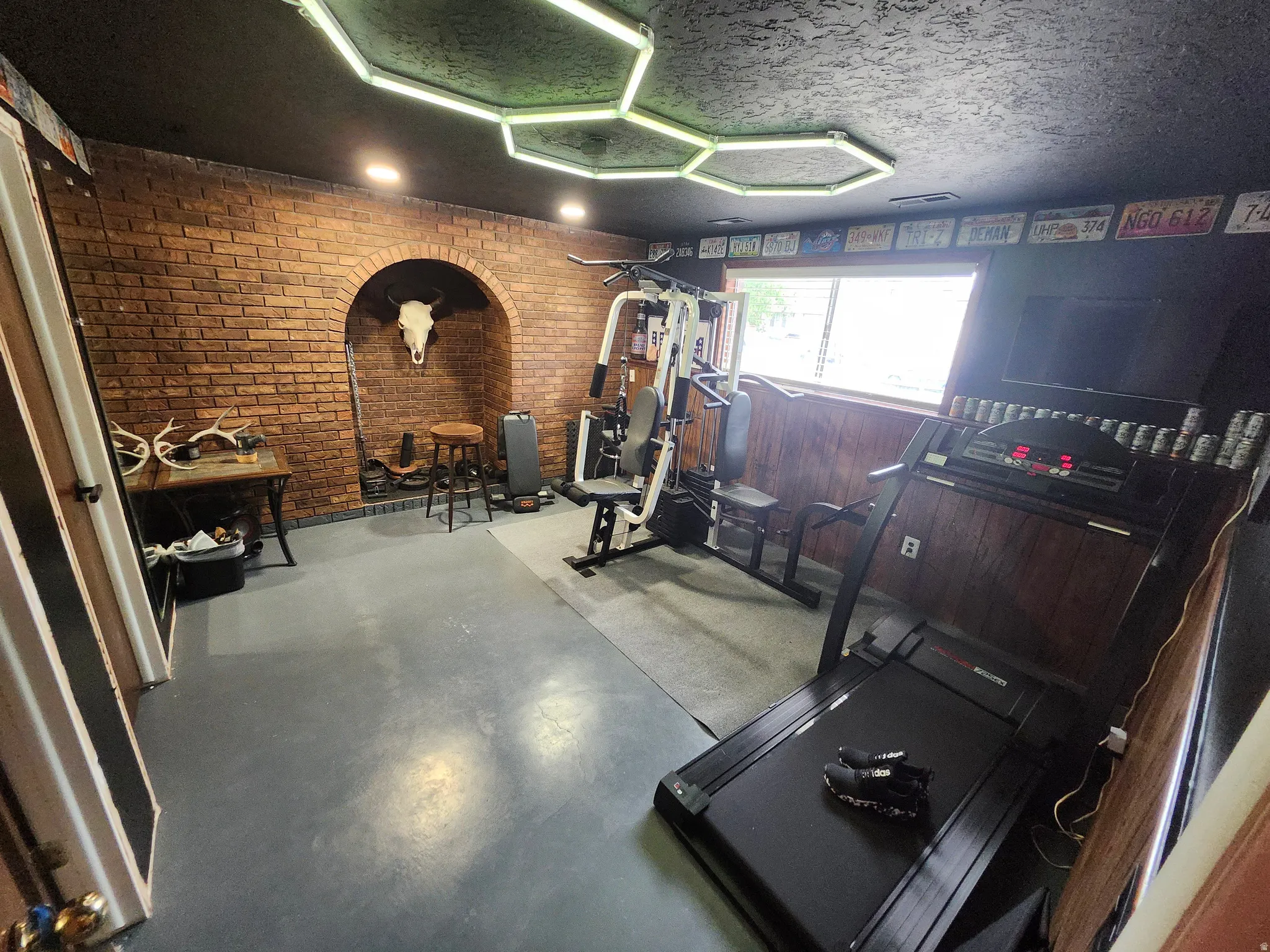 Room featuring brick-finish wall with an arched alcove, wood-finish paneling, and painted concrete flooring
