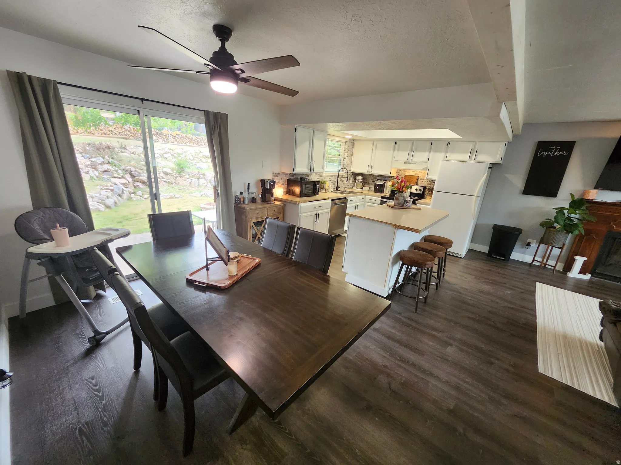 Open-concept living area featuring wood-finish flooring, a contemporary ceiling fan, and a kitchen with white cabinetry