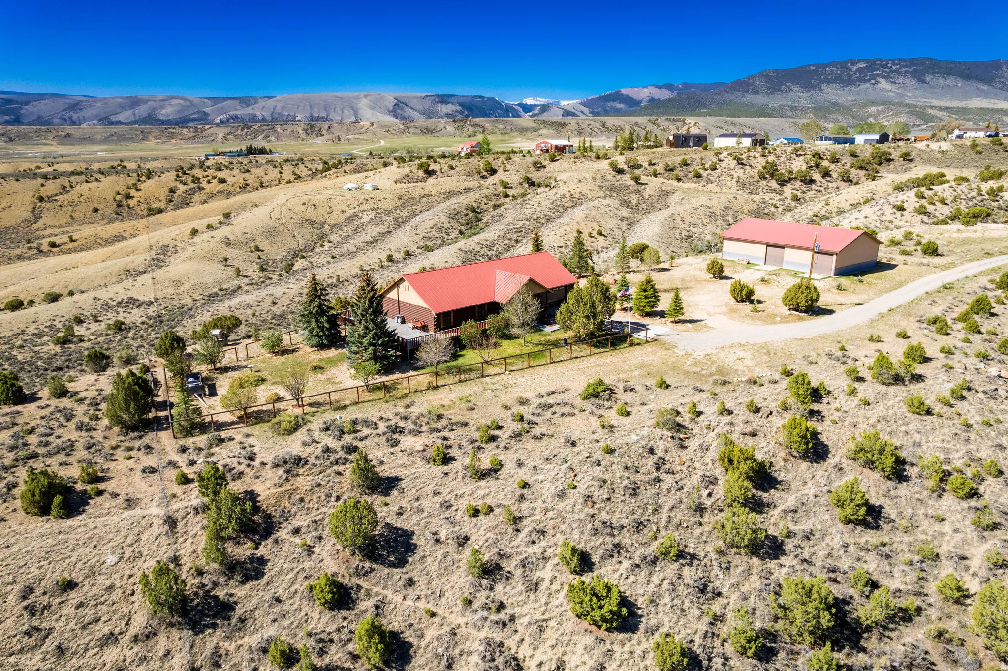 Expansive property featuring a residence with a red roof, a separate large outbuilding, and a gravel driveway