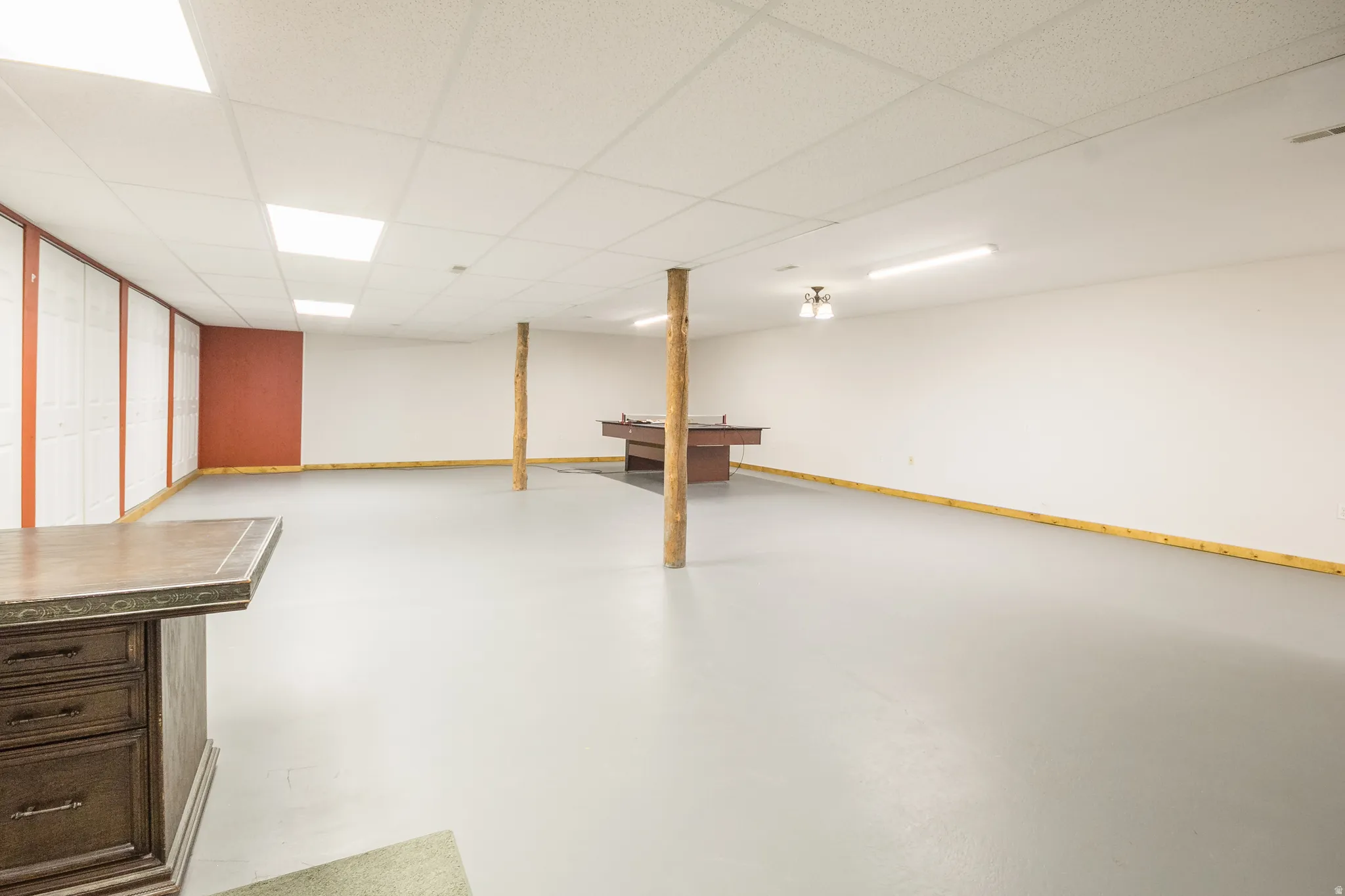 Spacious finished basement featuring a drop ceiling with recessed lighting, light gray flooring, and a built-in bar with a stone-finish countertop