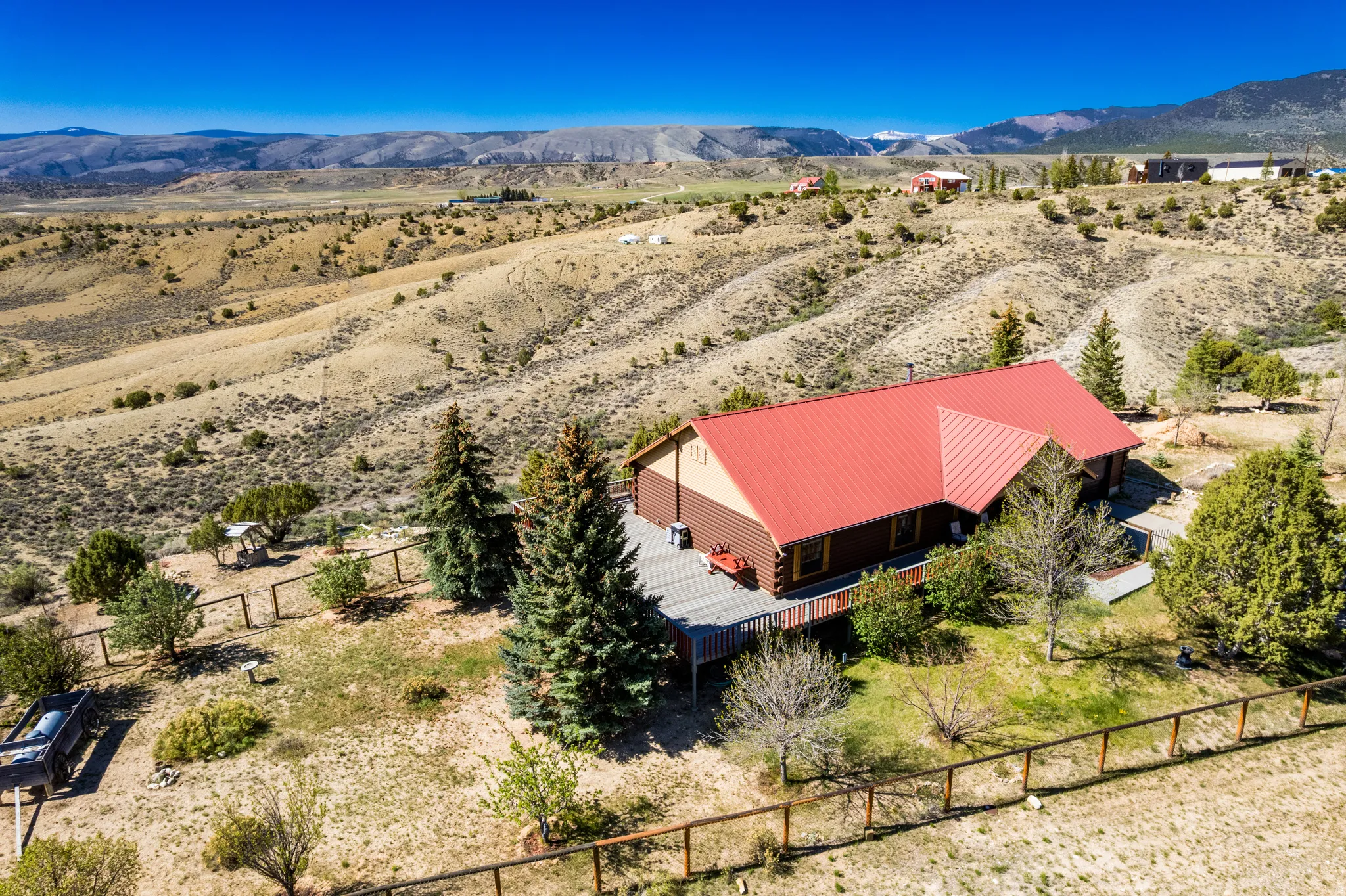Ranch-style residence featuring a prominent red metal roof, expansive wood deck, and surrounding natural landscaping