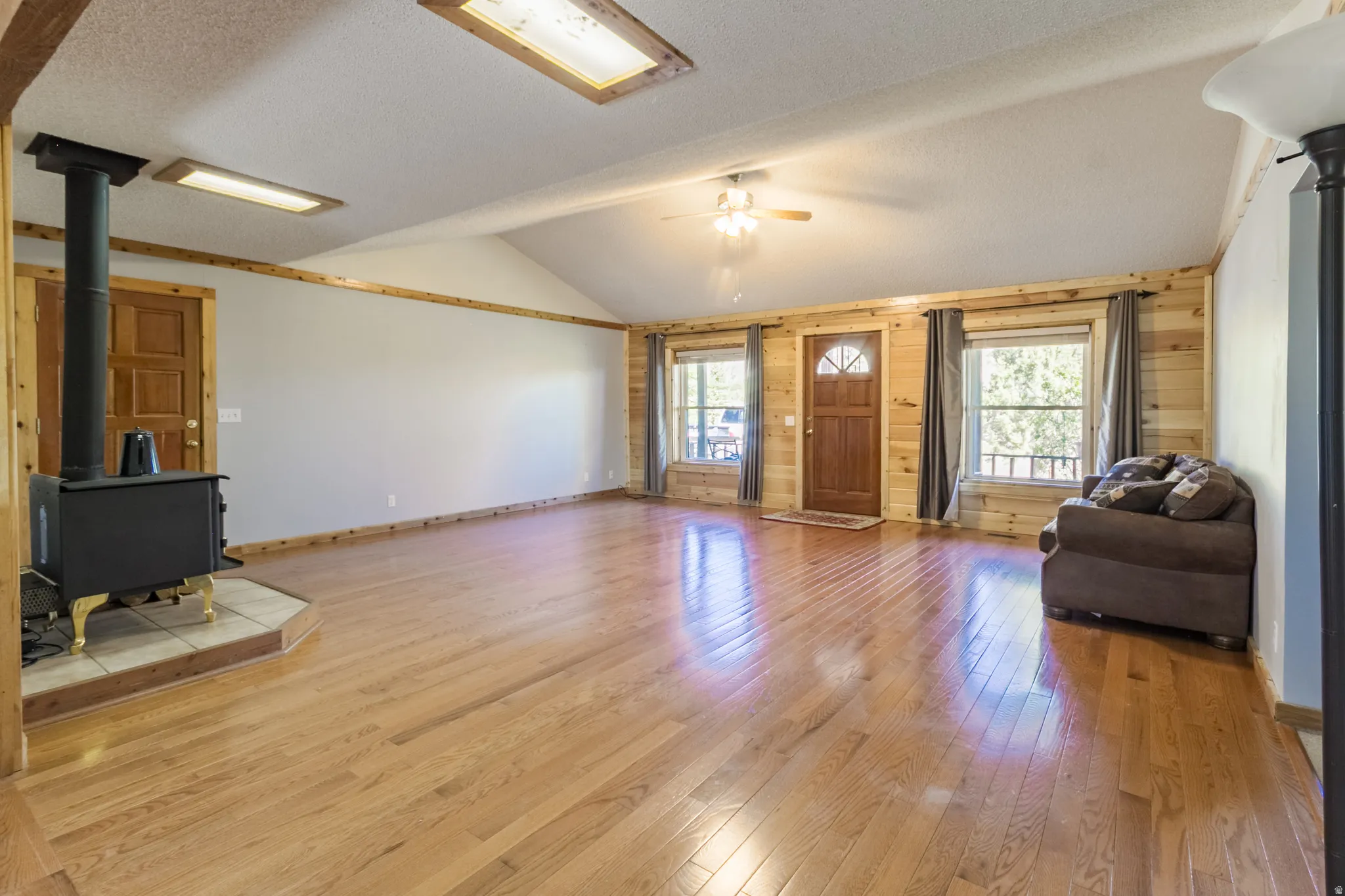 Spacious living area featuring wood-finish flooring, a vaulted ceiling, and a wood-burning stove on a tiled hearth