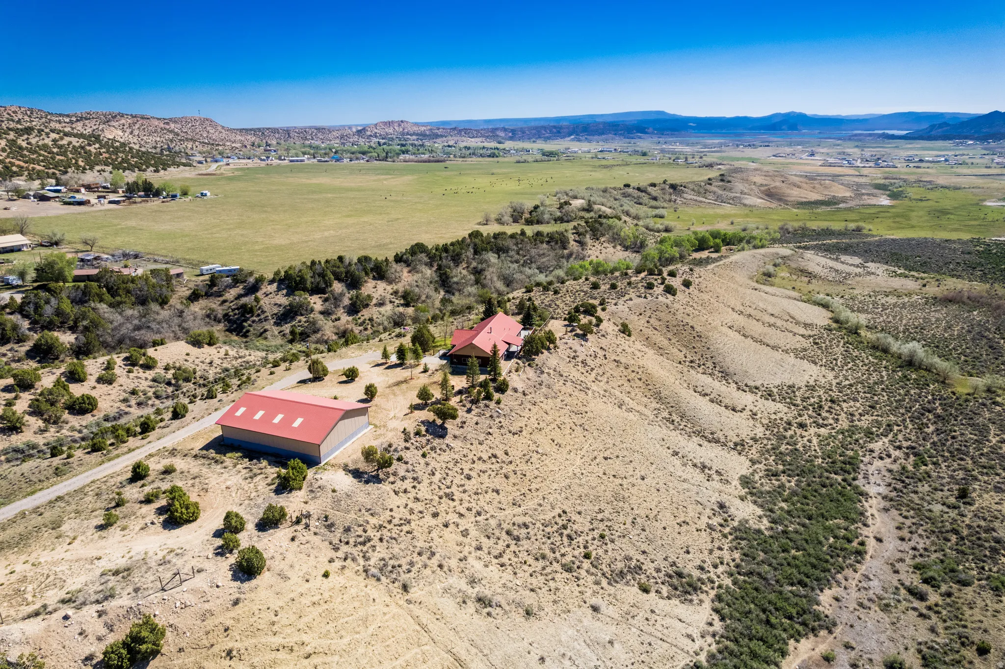 Expansive rural property featuring a primary residence with a red roof, a separate large outbuilding with a red metal roof, and a gravel driveway