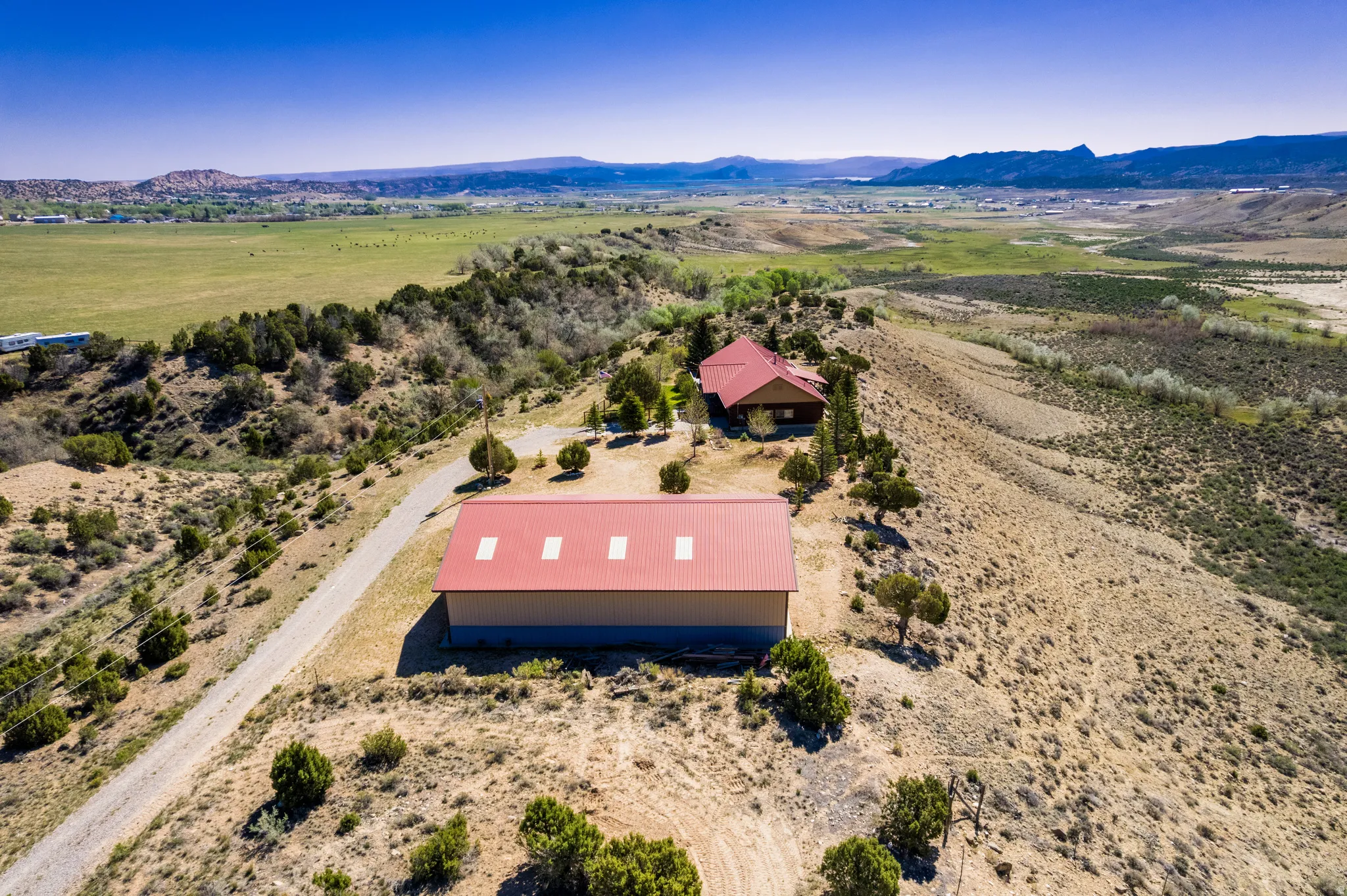 Expansive property featuring a large metal-roofed outbuilding, a residential structure with a red roof, and a winding gravel driveway