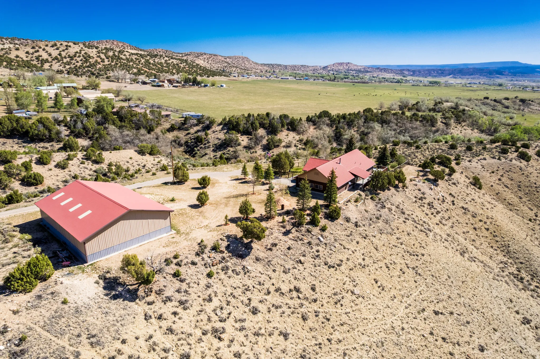 Expansive rural property featuring a primary residence with a red roof, a separate large metal outbuilding with a red roof, and natural desert landscaping