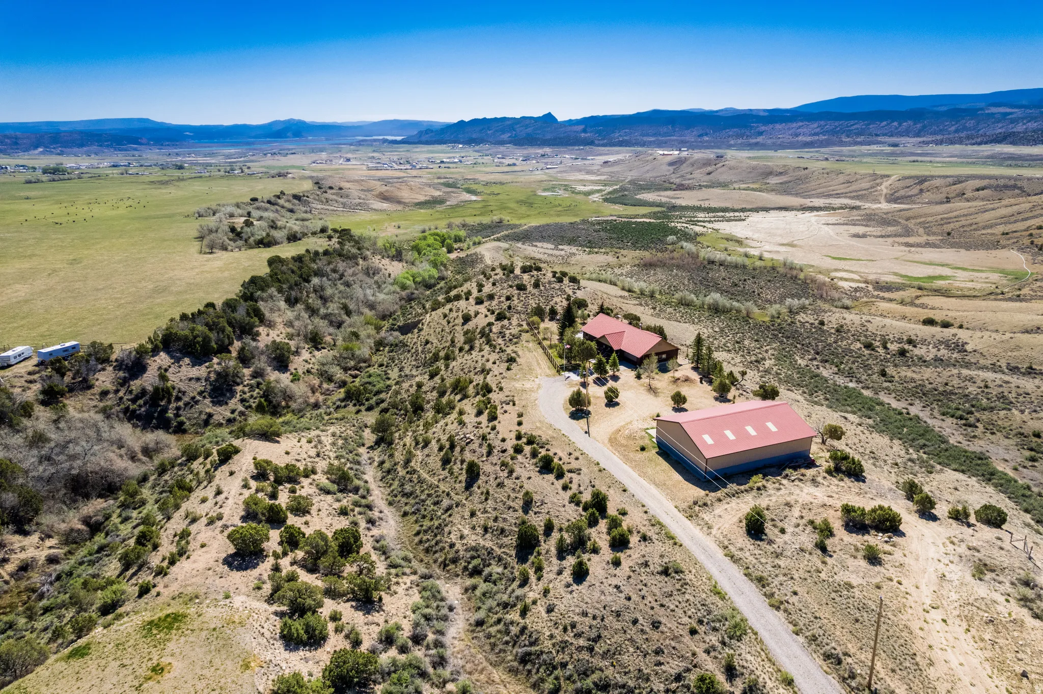 Expansive property featuring a main residence with a red roof, a large red-roofed outbuilding, and an unpaved driveway