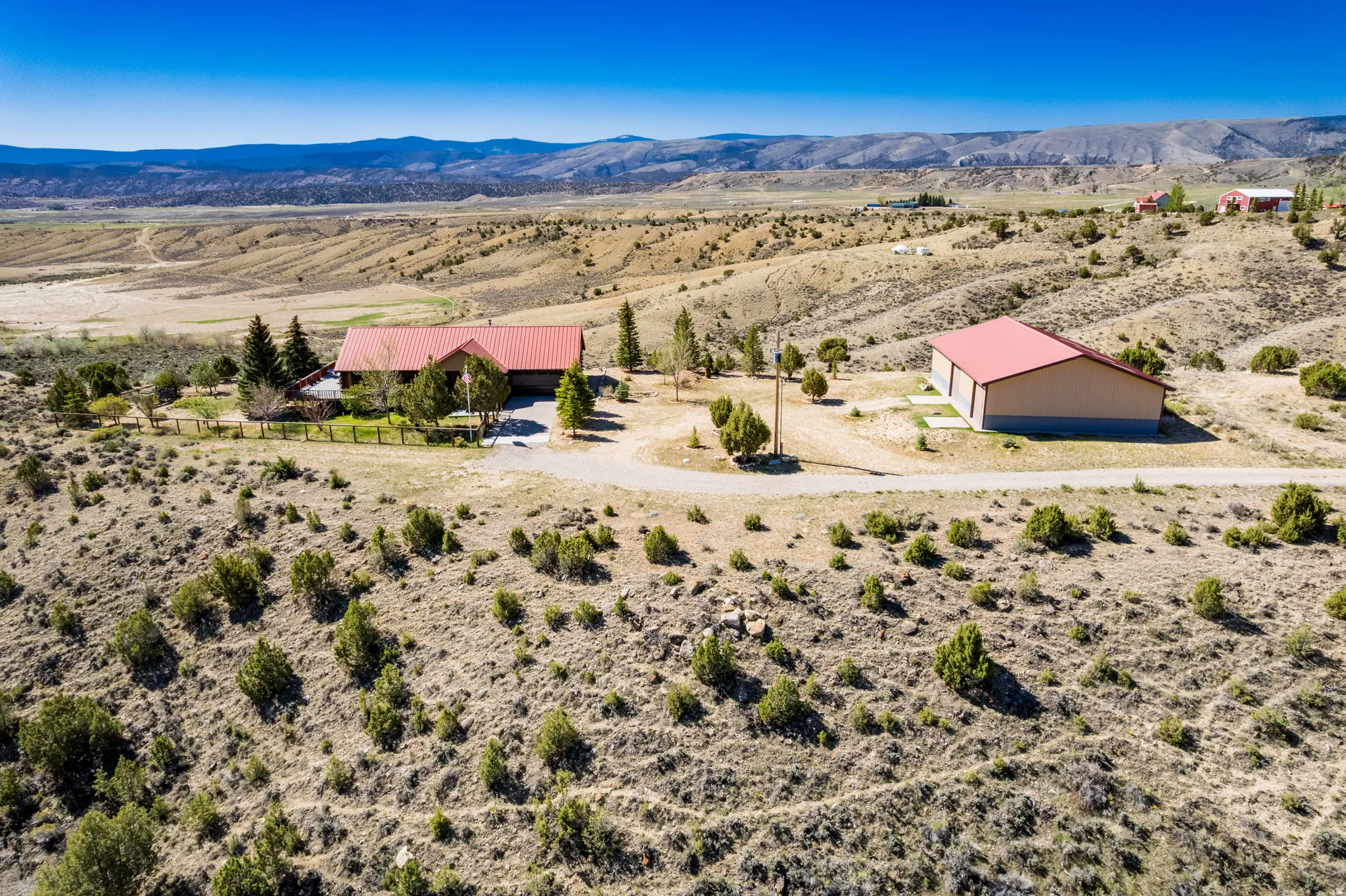 Expansive property featuring a residence with a red-toned roof, an accessory building with a matching red-toned roof, and a gravel driveway