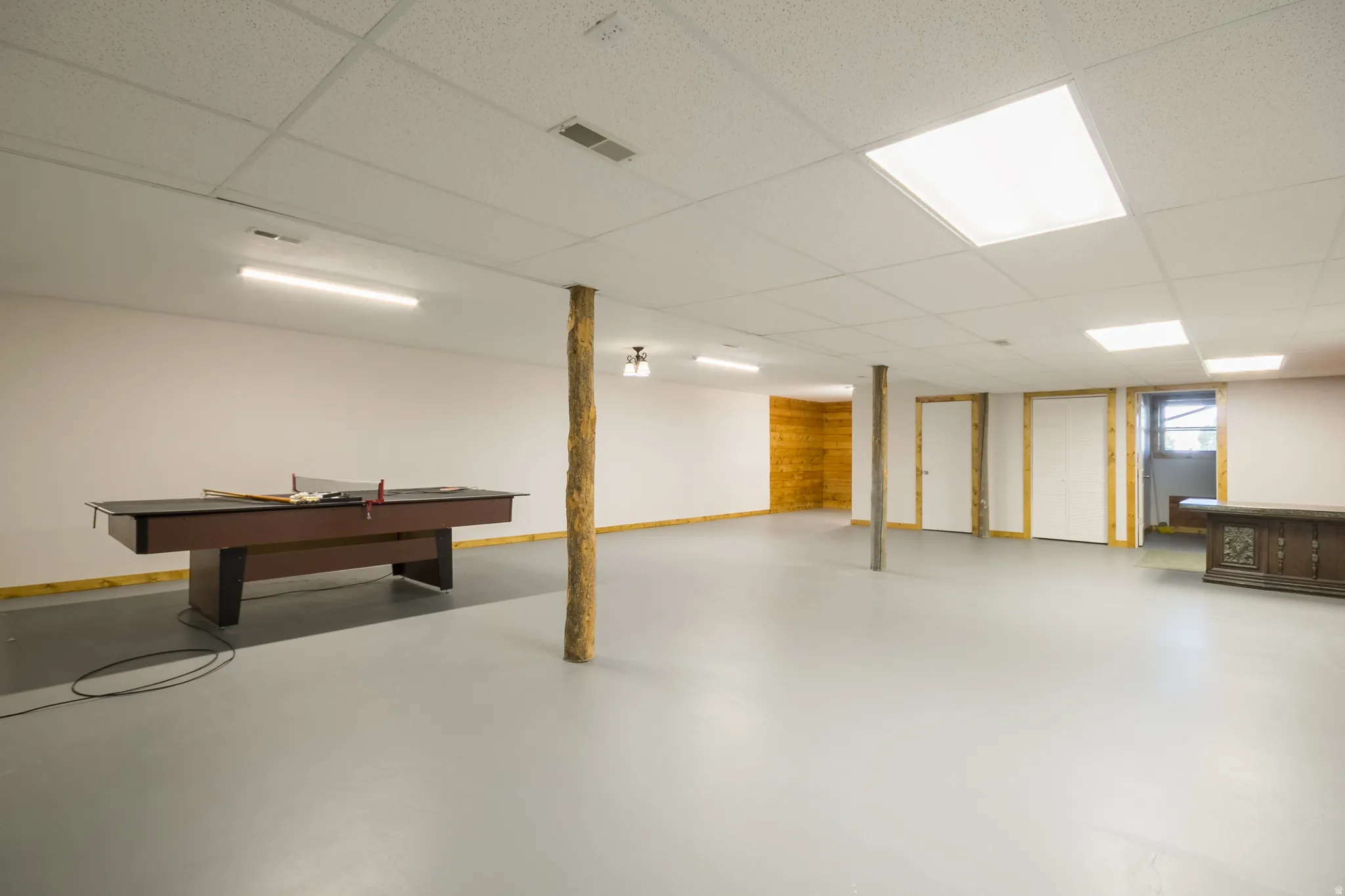 Spacious lower level featuring light gray flooring, white walls, and a suspended acoustic ceiling with integrated lighting