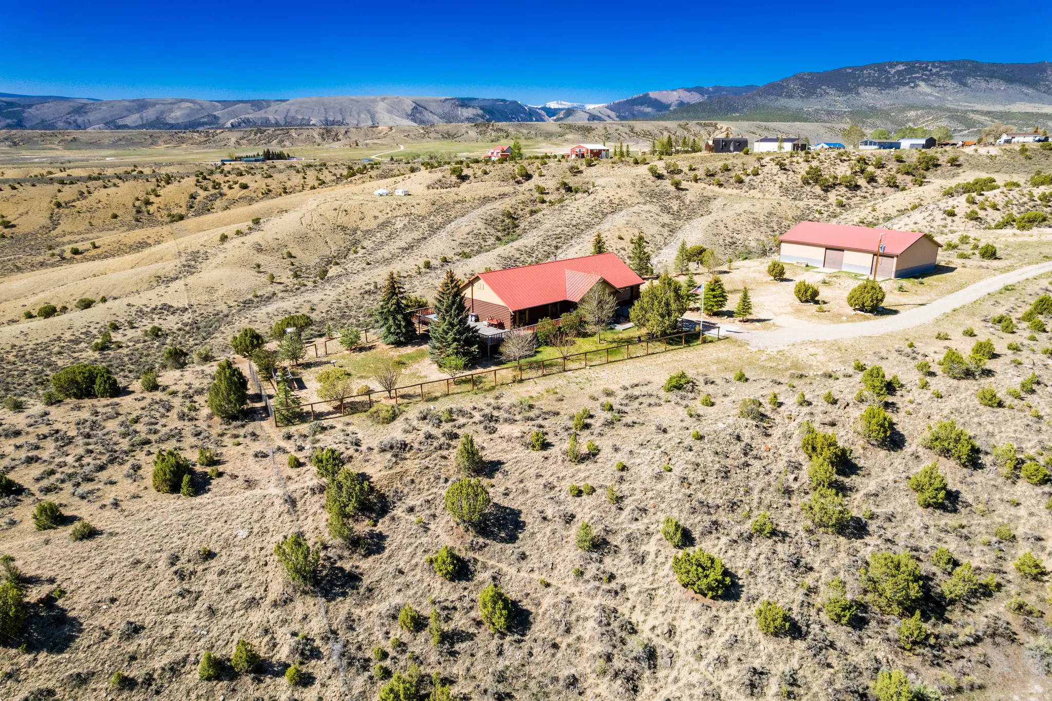 Expansive property featuring a red-roofed residence, a large detached red-roofed outbuilding, and a winding gravel driveway