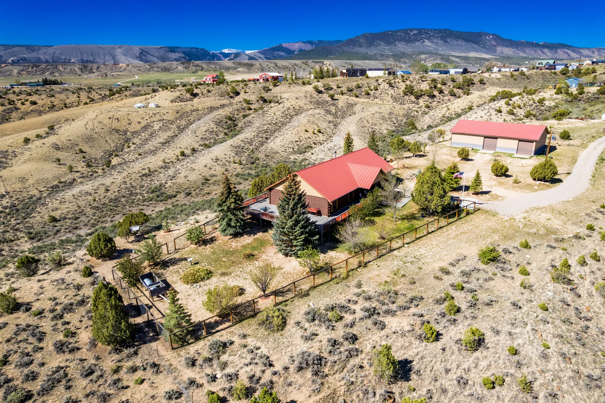Elevated property featuring a home with a red metal roof, surrounded by natural landscaping and mature evergreen trees