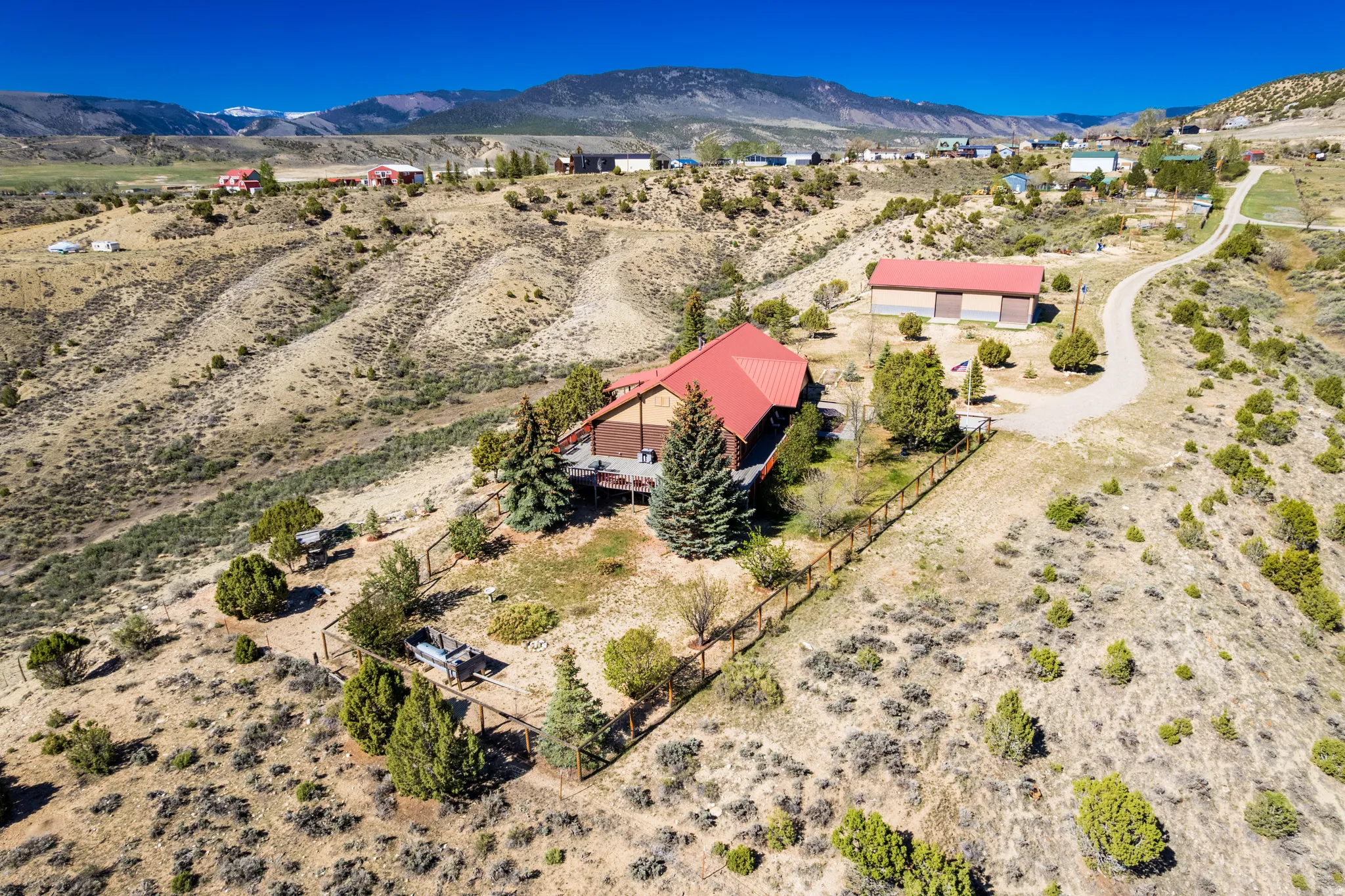 Mountain landscape featuring a house with a red roof, an expansive deck, and surrounding evergreen trees