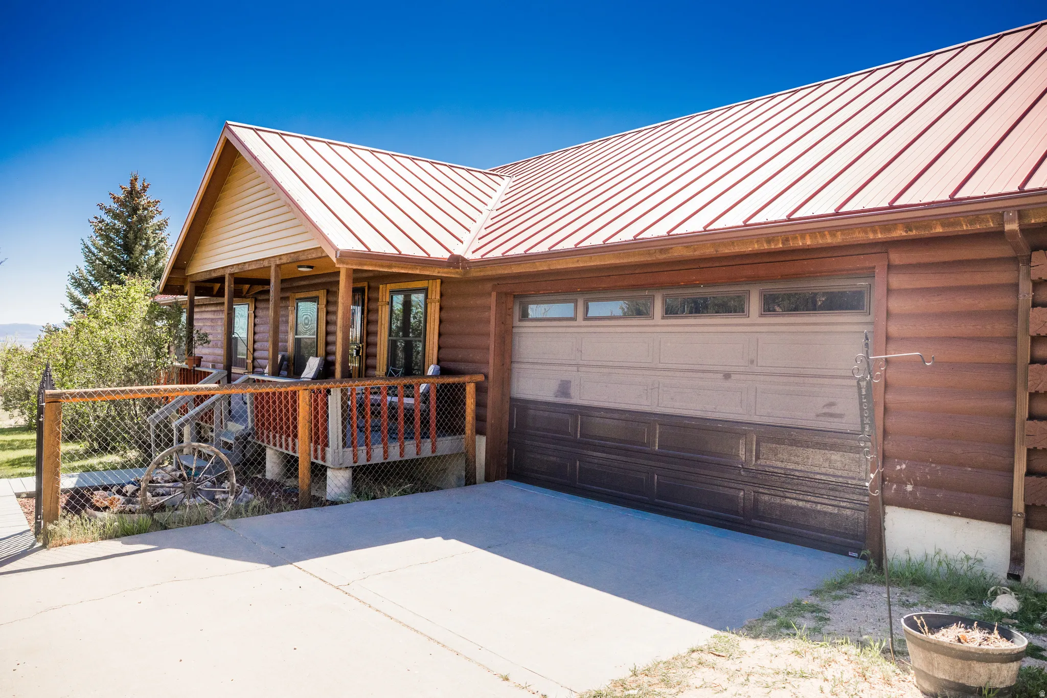 Log siding exterior featuring a red metal roof, covered porch, and attached garage