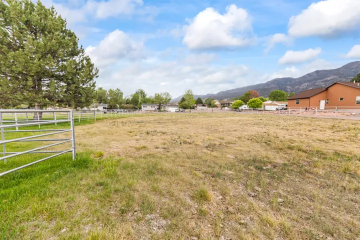 Expansive lot featuring a metal perimeter fence, mature trees, and mountainous terrain in the background