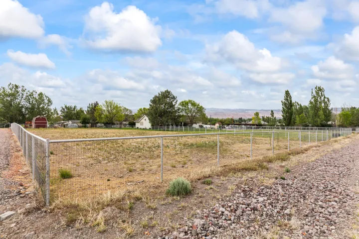 Expansive fenced parcel featuring a chain-link perimeter, unpaved access roads, and distant mountain scenery