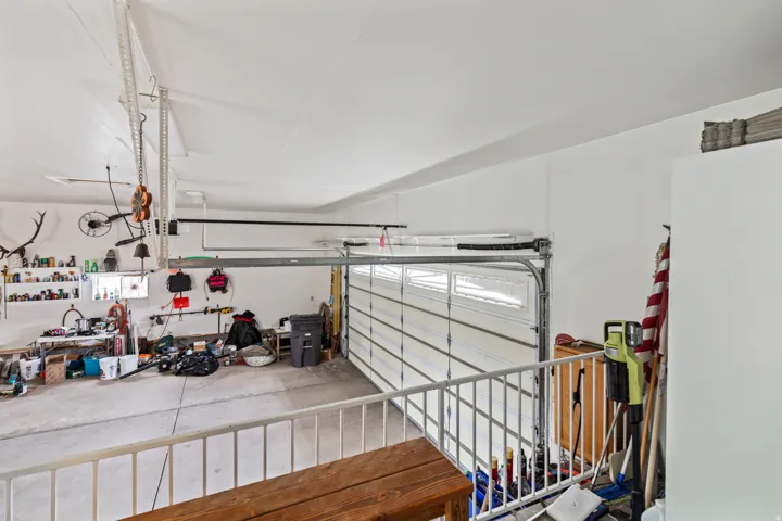 Two-story garage with a white sectional door, concrete flooring, and a white railing overlooking the garage space