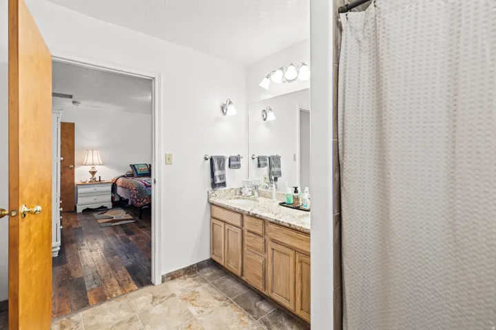 Bathroom featuring a double vanity with light wood cabinetry, a light-toned stone countertop, and two undermount sinks