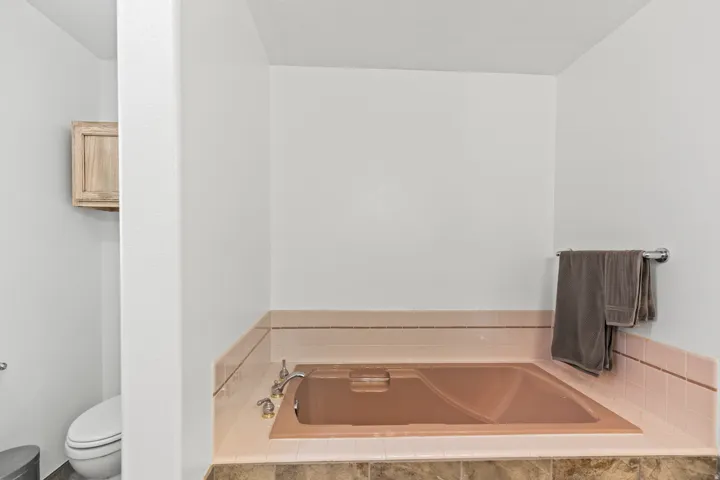 Built-in soaking tub with brass-toned fixtures, surrounded by pink accent tile and a contrasting mosaic tile base