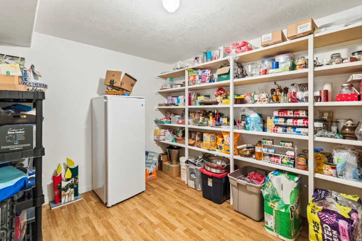 Spacious pantry featuring extensive built-in shelving, durable wood-finish flooring, and white walls