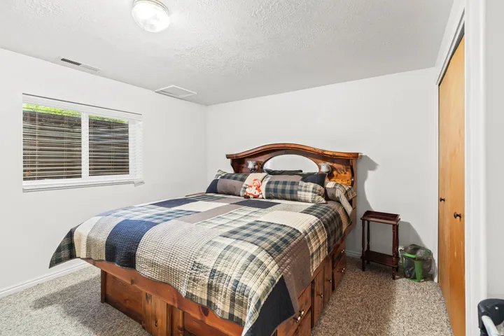 Bedroom featuring a standard window with blinds, light-colored carpeting, a ceiling-mounted light fixture, and a built-in closet with a wood-finish bifold door
