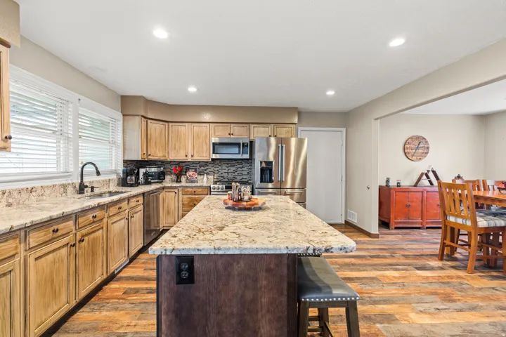 Kitchen featuring an island with stone-look countertop, wood-finish flooring, light-toned cabinetry, stainless steel appliances, and recessed lighting