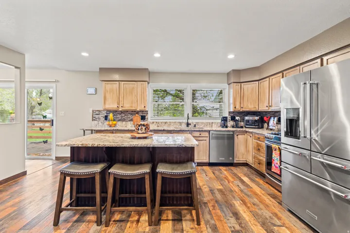 Spacious kitchen featuring wood-finish flooring, light wood cabinetry, and a central island with a stone-finish countertop