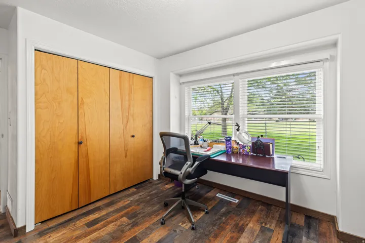 Room featuring wood-finish flooring, a large window with horizontal blinds, and a built-in closet with light wood doors