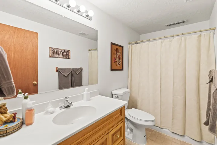 Bathroom featuring a wood-finish vanity with a white countertop and integrated sink, a large wall-mounted mirror, and overhead vanity lighting