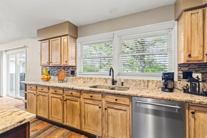 Kitchen featuring wood cabinetry, granite countertops, stainless steel dishwasher, dual basin sink with a gooseneck faucet, and a mosaic tile backsplash