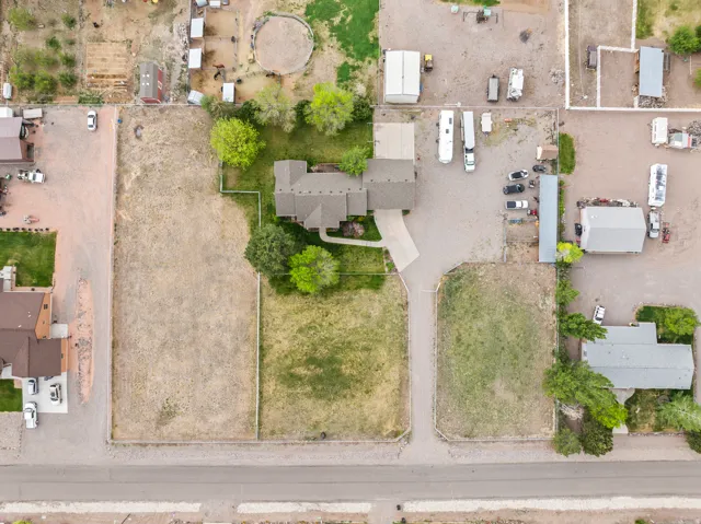 Expansive property featuring a central residence with a gabled roofline, a paved driveway, and established trees