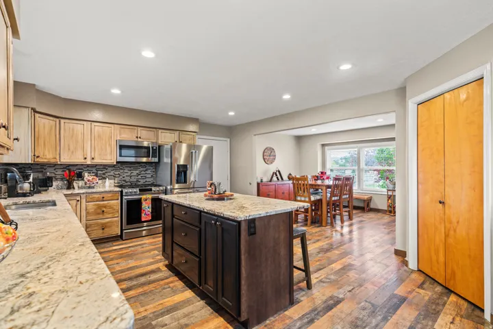 Kitchen featuring wood-finish flooring, two-tone cabinetry, stainless steel appliances, granite countertops, and recessed lighting