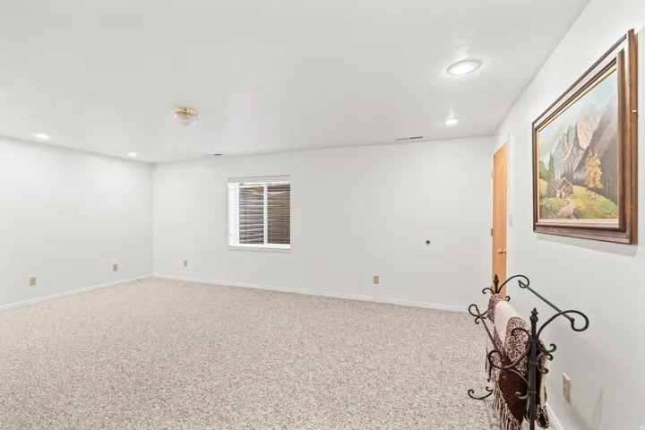 Spacious room featuring neutral carpeting, a white ceiling with recessed lighting, and a single window with blinds