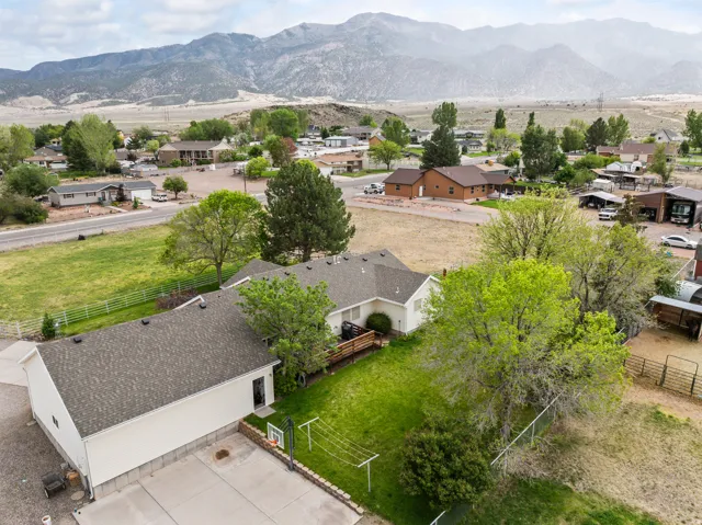 Expansive property featuring a detached garage, a concrete sports court, a fenced yard with mature trees, and a mountain backdrop