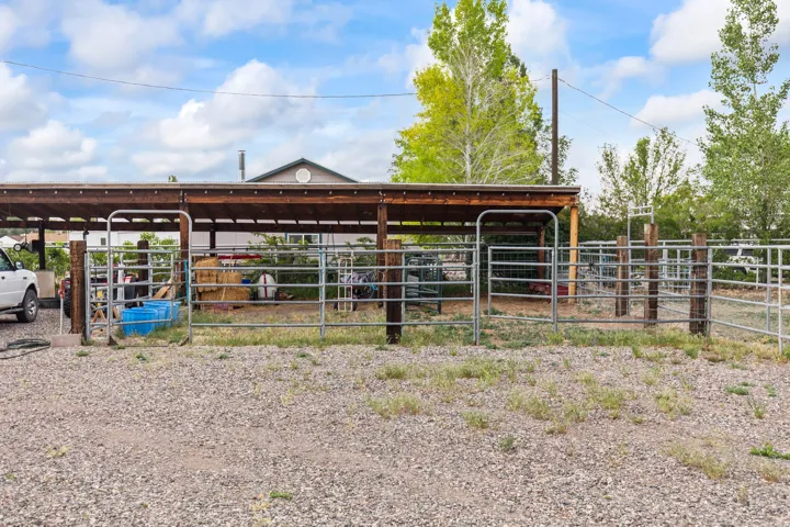 Gravel outdoor area featuring a wood-framed covered structure, metal fencing, and multiple gated sections