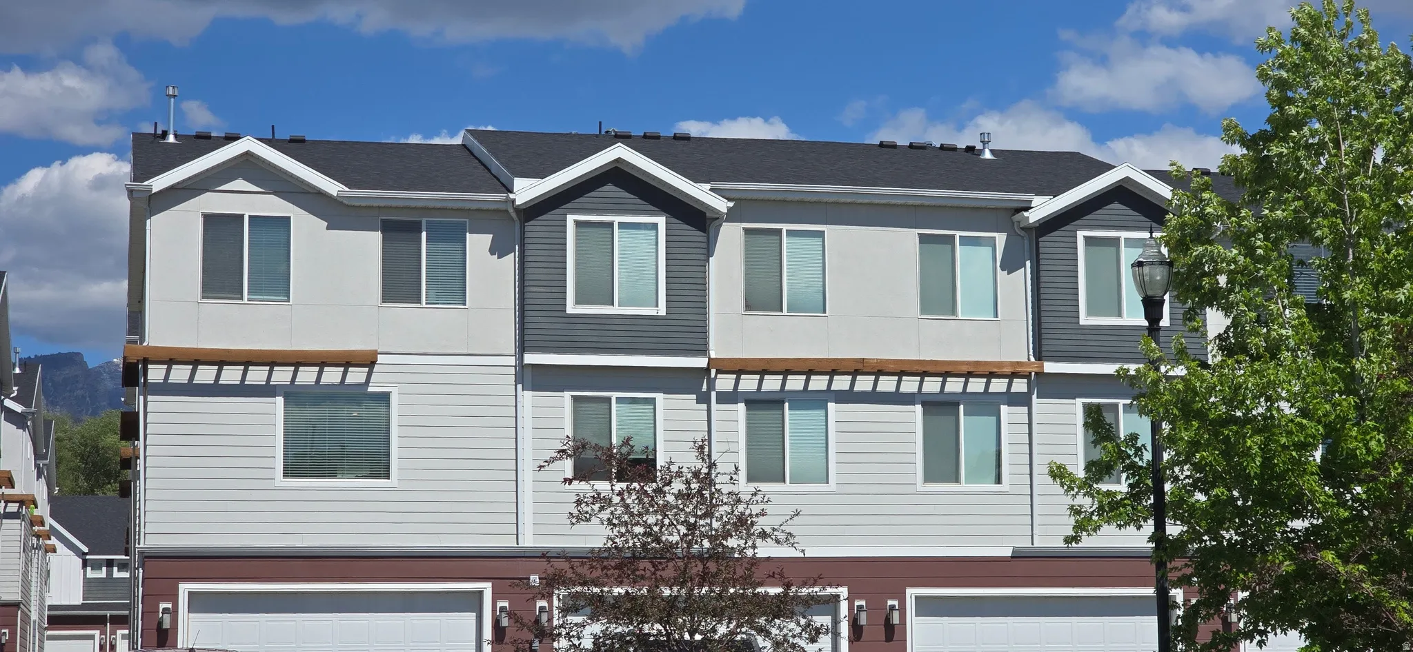 Modern townhome exterior with multiple garages, light-colored siding, dark gray accents, and a dark shingle roof