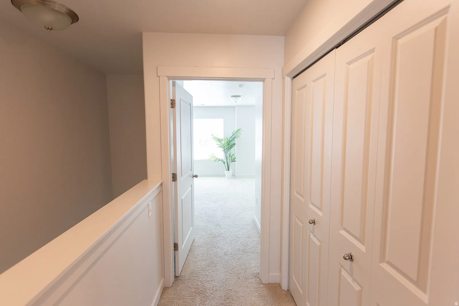 Carpeted hallway featuring a built-in closet with bi-fold doors, a recessed ceiling light fixture, and a white painted railing