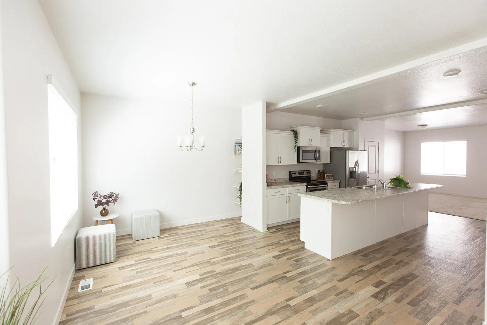 Open-concept living area featuring wood-finish flooring, a contemporary kitchen island with a stone-look countertop, white cabinetry, and stainless steel appliances