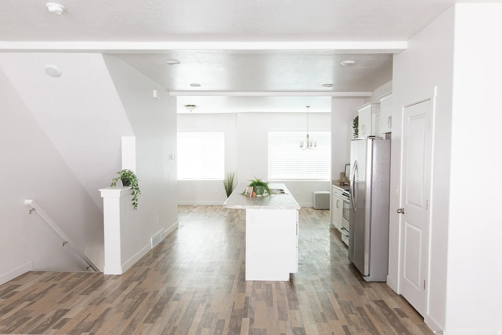 Open-concept interior featuring wood-finish flooring, a kitchen island with a stone-finish countertop, white cabinetry, and stainless steel appliances