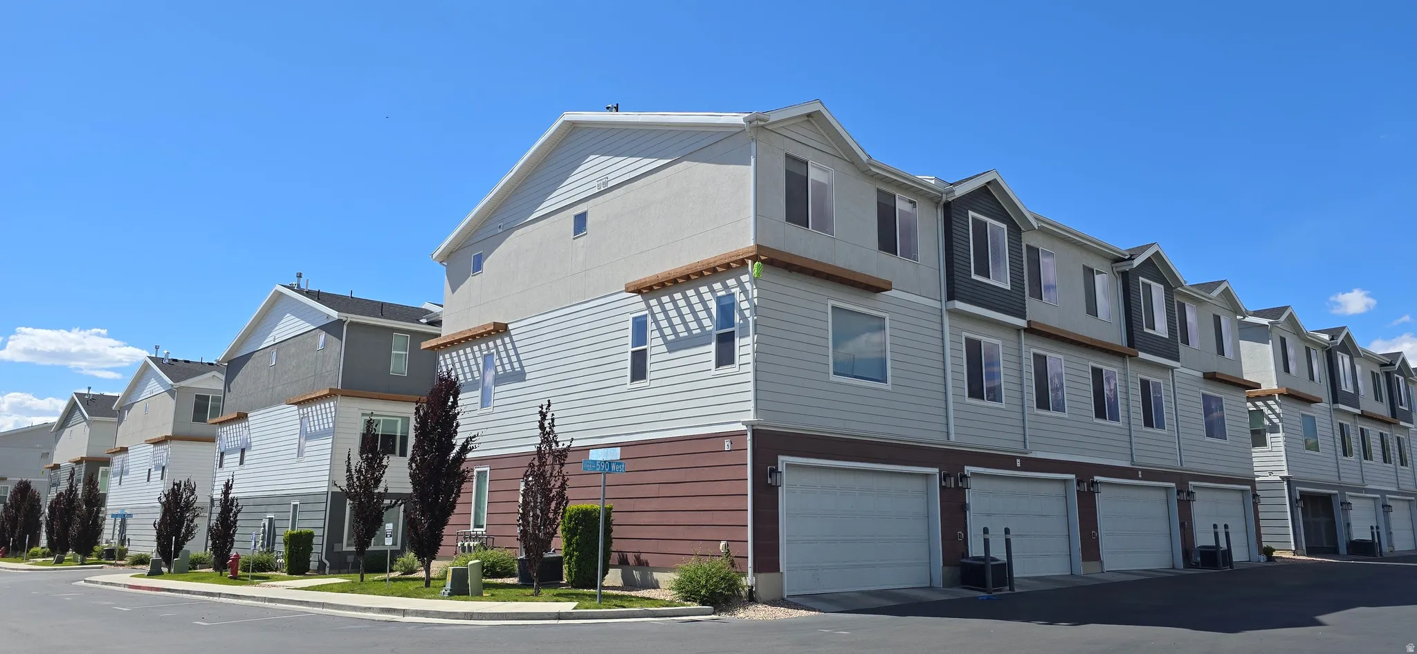 Modern townhome exteriors featuring multi-toned siding, attached garages, and mature landscaping