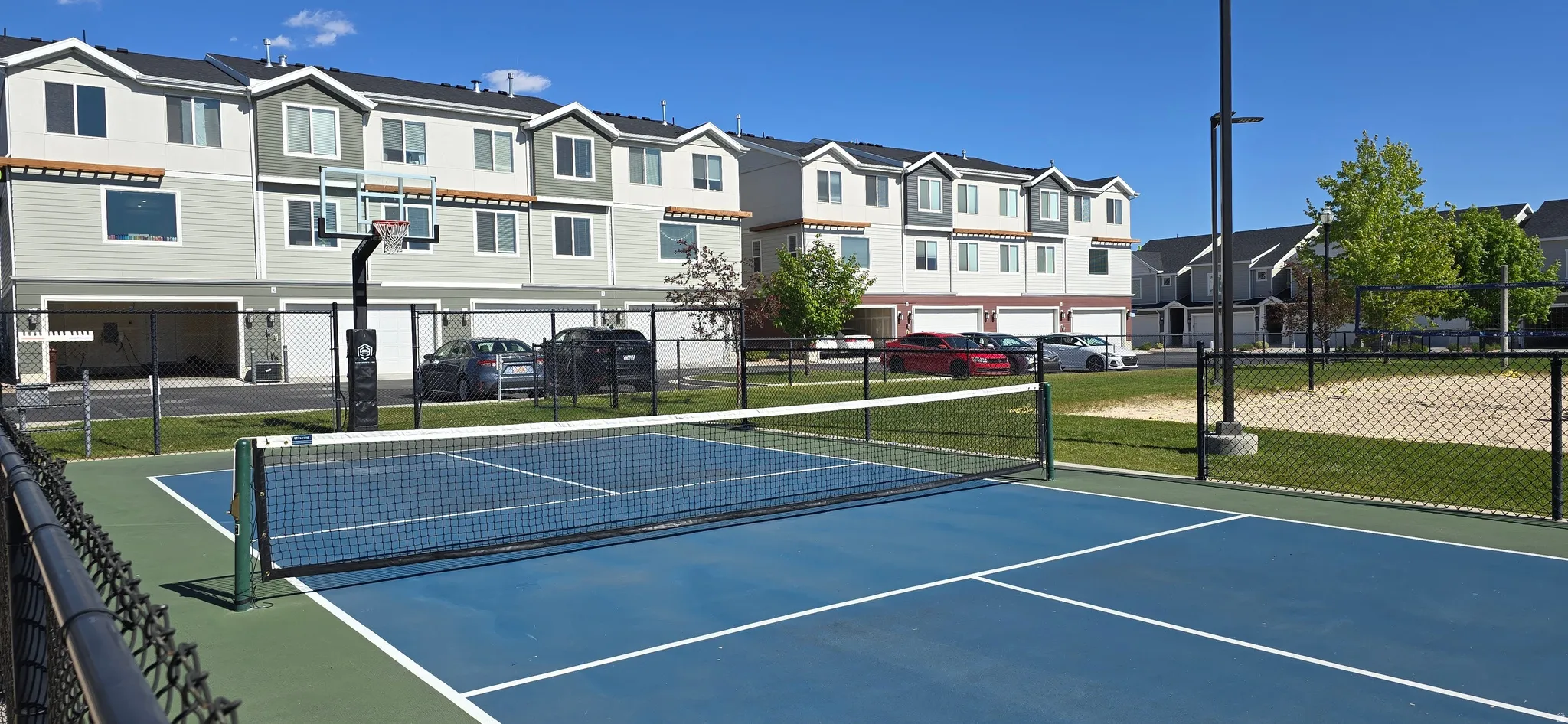 Fenced multi-sport court featuring a pickleball net and basketball hoop