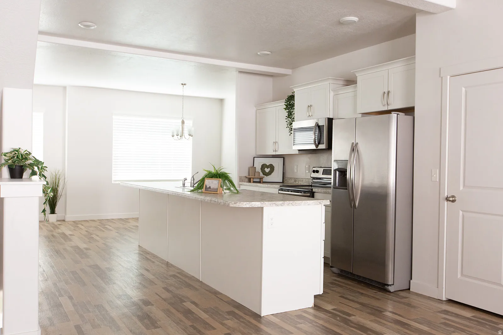 Kitchen featuring white cabinetry, stainless steel appliances, a large island with a light-toned countertop, wood-finish flooring, and recessed lighting