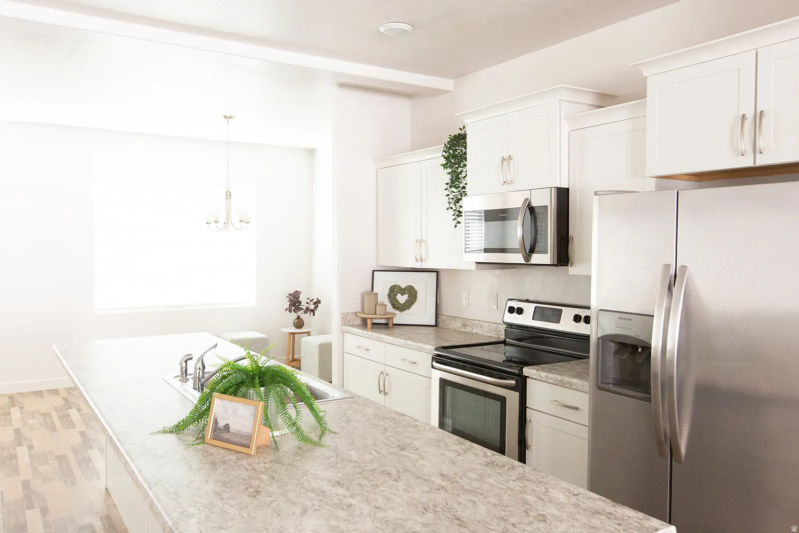 Kitchen featuring an expansive island with an undermount sink, white cabinetry, stainless steel appliances, and wood-finish flooring